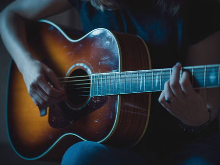A woman playing an acoustic guitar, showcasing her relaxed and focused expression in a moody setting.の素材