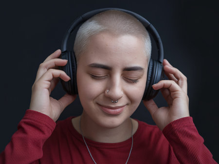 A young woman with short hair enjoying music with headphones, smiling in a cozy atmosphere.の素材