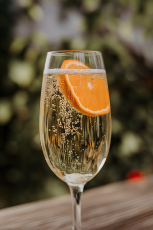 Sparkling beverage with a slice of orange in a glass, against a blurred green background.の素材