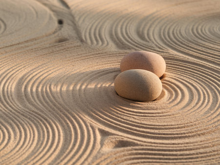 Two smooth stones resting on gently rippled sand, showcasing tranquility and harmony.の素材