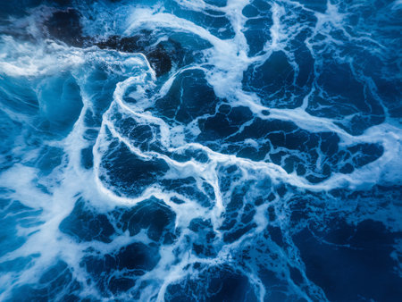 Aerial view of ocean waves creating patterns in vibrant blue and white foam.の素材