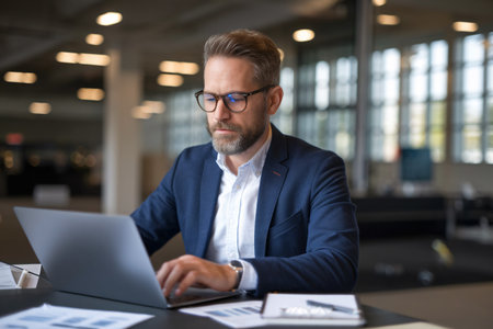 Focused middle-aged Caucasian man working on a laptop in a modern office space.の素材