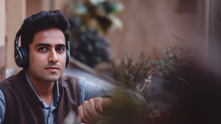 Young South Asian man wearing headphones, enjoying music in a serene outdoor setting.の素材