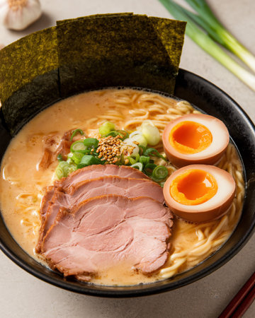 Delicious bowl of ramen with tender pork, soft-boiled eggs, and green onions on a neutral background.の素材