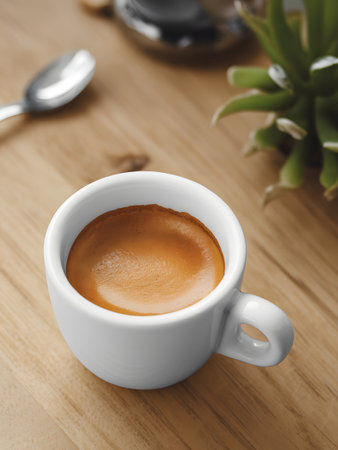 A close-up of a white espresso cup filled with rich brown coffee, surrounded by a wooden surface.の素材