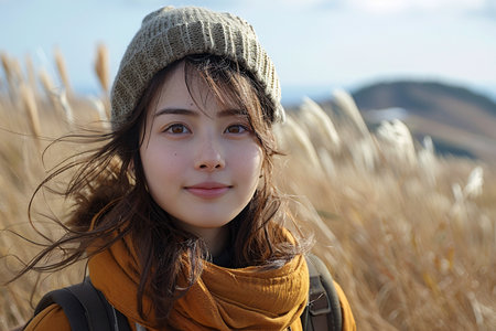 A young Asian woman with long hair enjoys a breezy day in a grassy field, smiling brightly.の素材