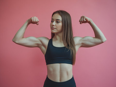 Young Caucasian female showing strength with arms flexed against a pink background.の素材