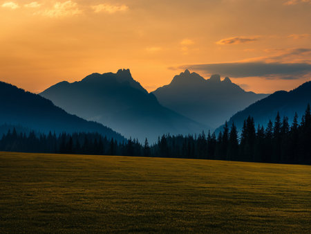 A tranquil sunset over majestic mountains surrounded by a lush green meadow.の素材