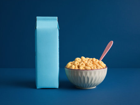 A bowl of cereal with a pink spoon next to a blue carton, set against a vibrant blue background.の素材
