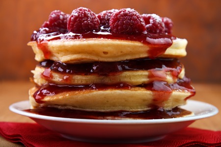 Warm baked pancakes with strawberry jam and fresh raspberry fruits on white plateの写真素材