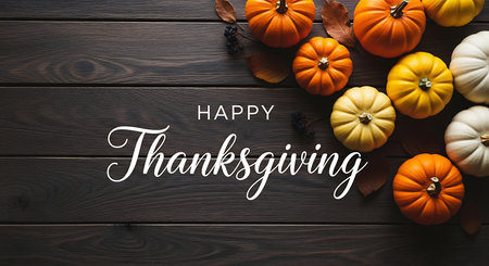 A warm and inviting Thanksgiving message is presented on a textured dark wood surface.  A scattering of vibrant orange, yellow, and white pumpkins and gourds adds seasonal charm.の素材