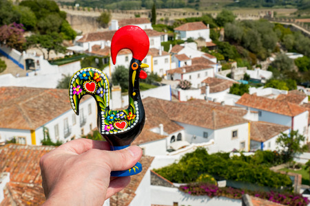 Male hand holds a Rooster of Barcelos (Galo de Barcelos) above Obidos. Portugalの写真素材