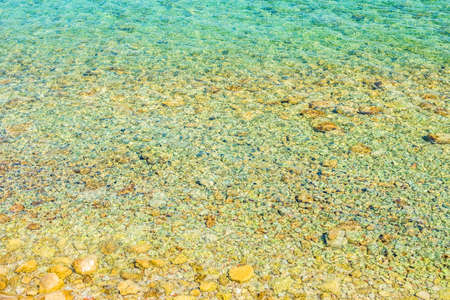 Stones in water. Stony beach. Colorful reflections on the water.