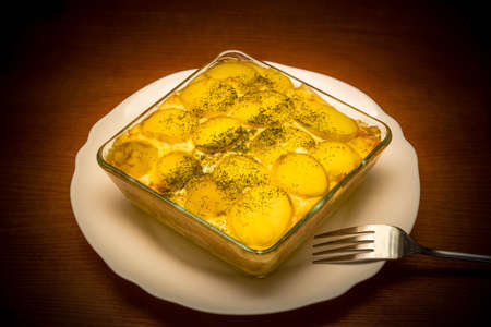 Potato casserole. Done vegetarian dish. Food in a glass dish on a plate and fork. Dinnerware set.の写真素材
