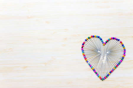 Heart arranged with colorful pins on a wooden background.の写真素材