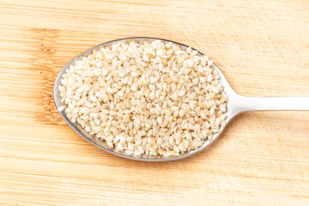 Sesame seeds on a wooden spoon lying on a wooden chopping board.の写真素材