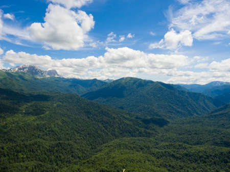 Aerial photo. Beautiful mountain valley. Summer landscape with mountain peaks covered with snow, cloudy sky and a segment of the road through the oak forest. Caucasus mountain system. Russia.の写真素材