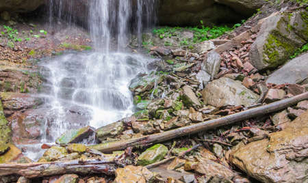 Large boulders and logs at the foot of the waterfall. Selective focus.
