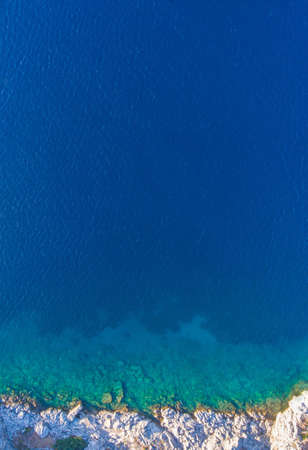 Conceptual sea background. Clean clear water is bordered with rocks on the shore. Aerial view.の写真素材