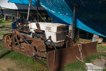 A small old abandoned bulldozer is rusting in a yacht yard.