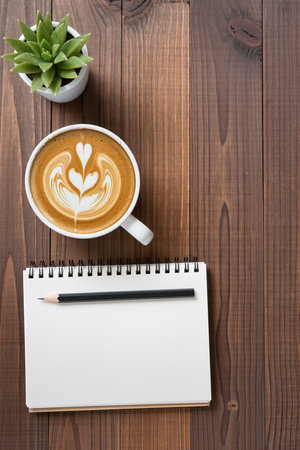 Cup of coffee latte art with notebook and pencil on wooden backgroundの素材