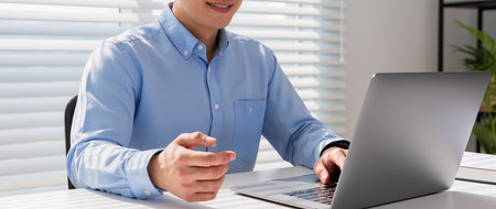 Cropped image of young businessman working on laptop computer at office deskの素材