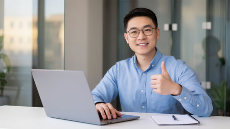Portrait of young asian businessman using laptop and showing thumbs upの素材