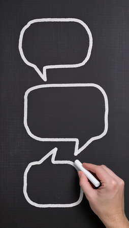 Hand drawing a speech bubbles on a blackboard with a white chalkの素材