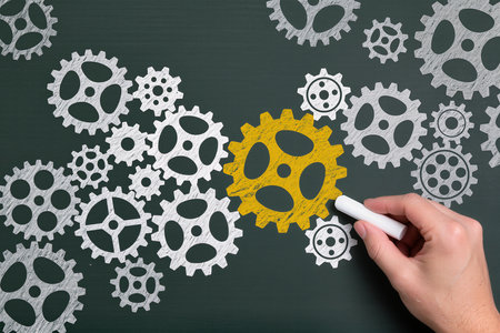 Business concept on blackboard with a human hand drawing a gear wheelの素材