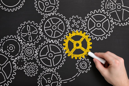 Hand drawing gear wheels on blackboard with white chalk, teamwork conceptの素材