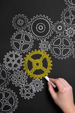 Hand drawing gear wheels on blackboard with white chalk, concept of teamworkの素材