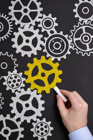 Hand drawing a gear wheel on a blackboard with a white chalkの素材