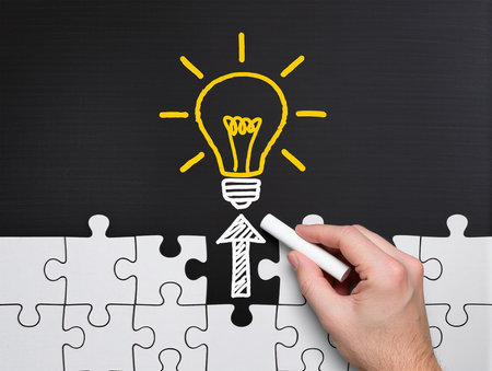 Hand drawing a light bulb with white chalk on a jigsaw puzzleの素材