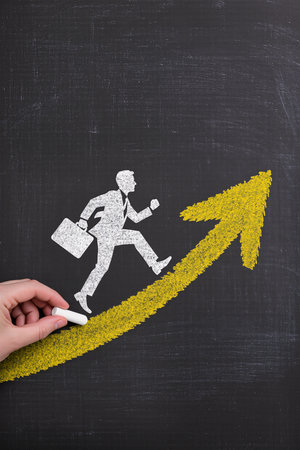Businessman running on a chalkboard with a yellow arrow pointing upの素材