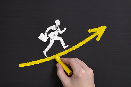 Businessman drawing a growing graph on blackboard with a yellow markerの素材