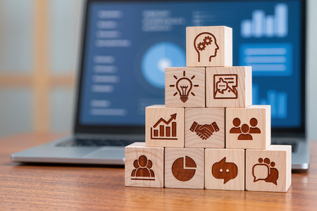 Wooden cubes with business icons on a desk in front of a laptopの素材