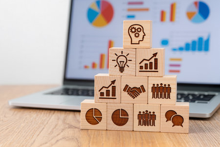 Wooden cubes with business icons on the background of a laptop.の素材