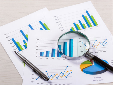 financial chart with magnifier and pen on wooden table, business conceptの素材