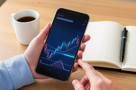 Smartphone screen displaying stock market data on a screen with a notebook and a cup of coffeeの素材