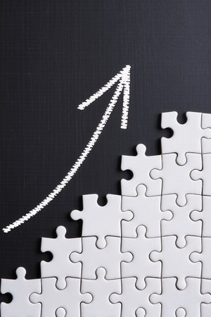 Top view of white jigsaw puzzle with upward arrow on black backgroundの素材