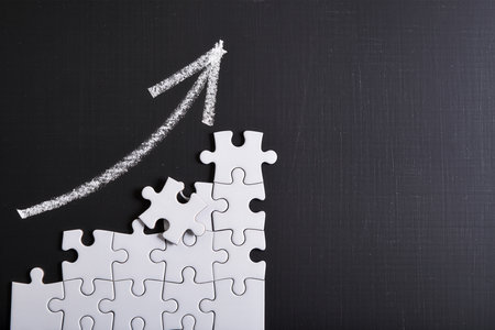 Top view of white jigsaw puzzle with arrow on blackboard backgroundの素材