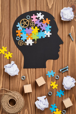 Human head with brain made of puzzle pieces and tools on wooden backgroundの素材