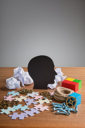 Human head made of puzzle pieces and gears on wooden table over grey backgroundの素材