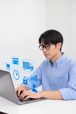 Young Asian man using laptop with social media icons on white background.の素材