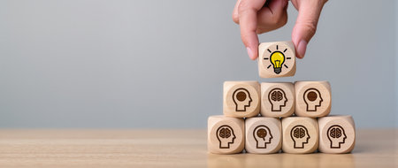 Hand arranging wooden cube with light bulb icon and human head icon on top, business idea conceptの素材