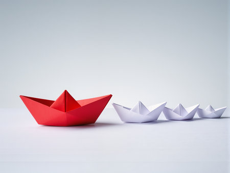Leadership concept with red paper ship leading white origami ships on white backgroundの素材