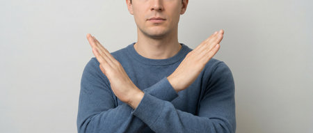 young man showing stop gesture with both hands, isolated on gray backgroundの素材