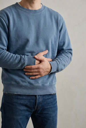 Unhealthy eating nutrition concept. Cropped closeup photo of unhappy sad guy touching left side feeling severe pain isolated grey backgroundの素材
