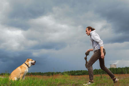 Tall man playing with big dog cadebou in a meadow. Cloudy sky and trees backgroundの写真素材