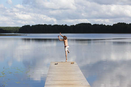 A man jumping from an old wooden jetty at a lakeの写真素材